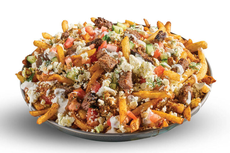 Loaded fries topped with steak, feta, tomato, cucumber, herbs, and creamy sauce on a white background.