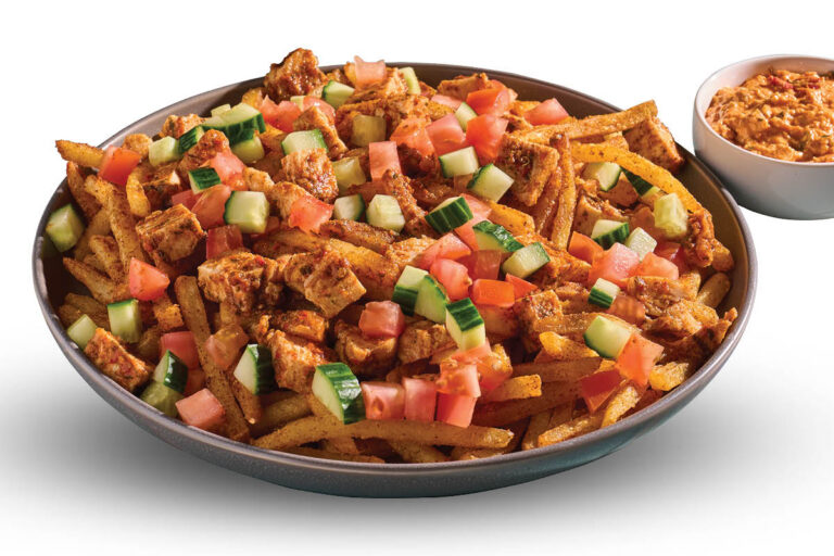 Loaded fries topped with seasoned chicken, tomato, cucumber, and sauce, with a dip cup on the side.