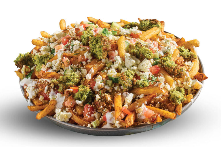 Loaded fries topped with falafel, feta, tomato, cucumber, and creamy sauce on a white background.